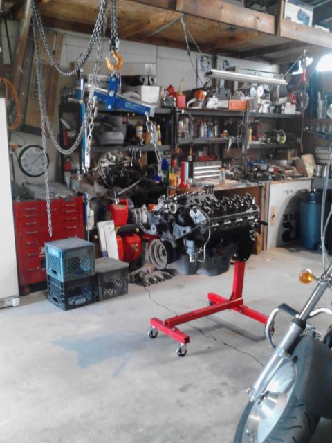 1978 Ford Bronco - An engine is mounted on a red stand in a cluttered garage workshop.