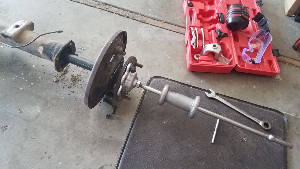 Rear axle assembly with brake drum and hub, attached to a slide hammer. Tools and a red toolbox are nearby