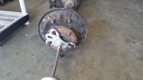 1985 Ford Bronco - A rear axle assembly with a brake drum and a tool is shown on a concrete floor.