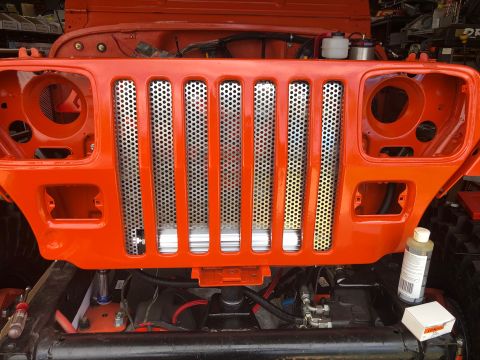 1992 Jeep Wrangler - Front end of an orange Jeep Wrangler undergoing reassembly, showing the distinctive grille and headlight openings.
