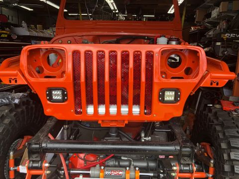 1992 Jeep Wrangler - Front view of an orange Jeep Wrangler undergoing reassembly, a custom grille and auxiliary lighting.