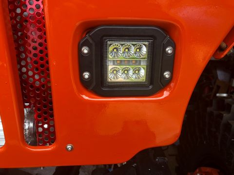 1992 Jeep Wrangler - Aftermarket LED light installed on the fender of an orange vehicle, near a red mesh grille.