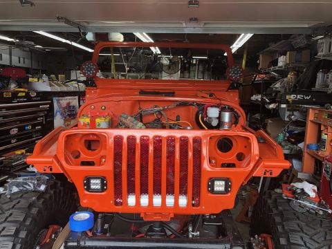 1992 Jeep Wrangler - This orange Jeep Wrangler is in a garage, undergoing some work with its grille removed and engine bay visible.