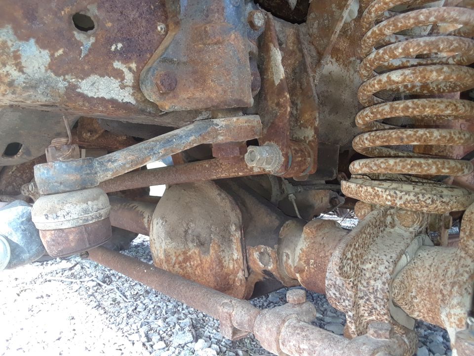 Heavily rusted front axle, steering linkage, and coil spring of a vehicle