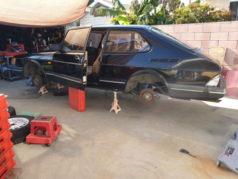 1991 Saab 900 - A black 1991 Saab 900 is elevated on jack stands in a garage, with its doors open, suggesting repair work.