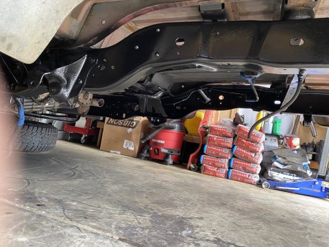 1994 Ford Bronco - The underside of a vehicle frame, possibly undergoing maintenance or repair, with various tools and supplies in the background.