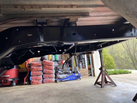 1994 Ford Bronco - The frame of a vehicle is elevated on jack stands, with a shop vac and floor jack visible in the background.