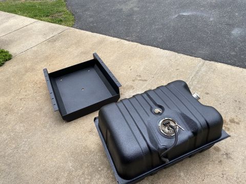 1994 Ford Bronco - A black fuel tank and its associated mounting bracket are shown resting on a concrete surface.