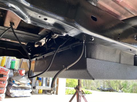 1994 Ford Bronco - The underside of a vehicle shows a freshly painted fuel tank and associated lines, with some construction materials in the background.