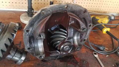 1985 Ford Bronco - Differential housing and gears are disassembled on a workbench, with tools nearby.