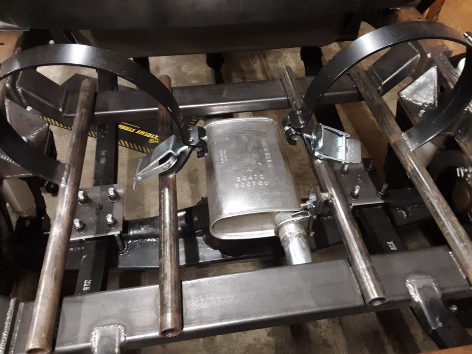 Close-up of a vehicle's muffler and exhaust pipes, with metal brackets and straps holding it in place