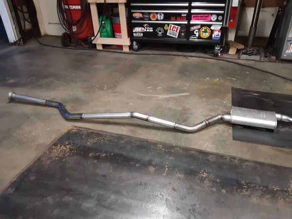 Exhaust system with muffler, laid out on a dark surface