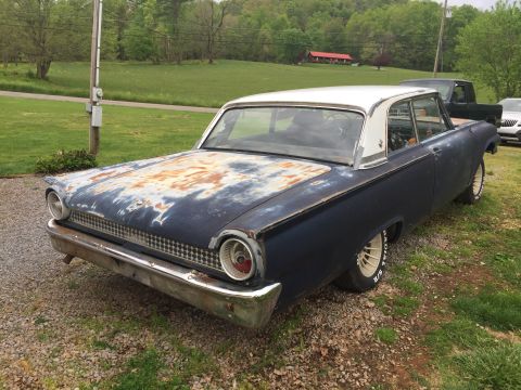 1961 Ford Galaxie - This vintage sedan, possibly a 1960 model, sits in a grassy area with a wooded background and another vehicle visible.
