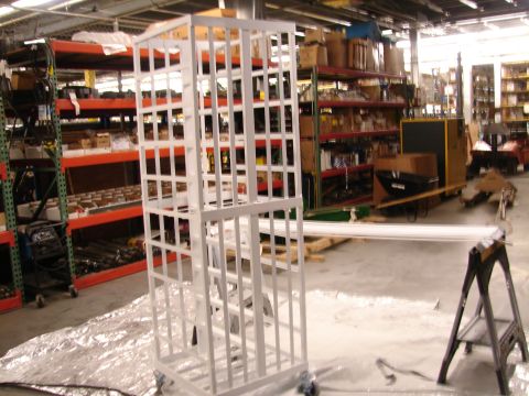 1973 Ford Ranchero - A white metal cage on wheels is positioned in a warehouse aisle with shelves of parts in the background.