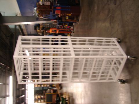 1973 Ford Ranchero - A white metal cage with wheels is shown in a warehouse environment, with shelving and equipment in the background.
