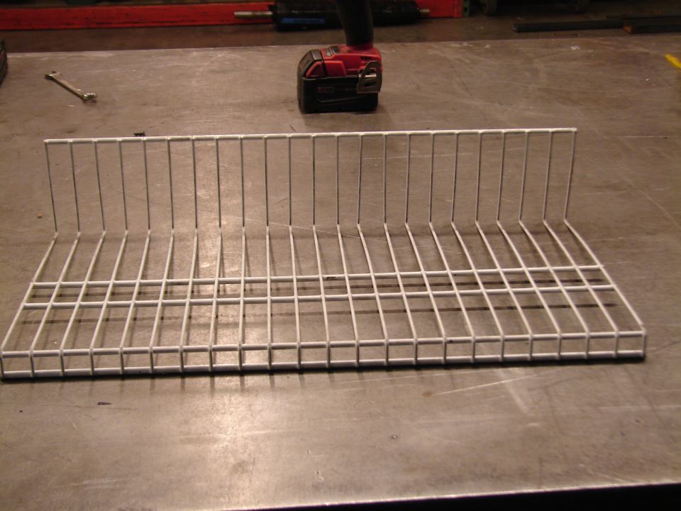 White wire rack on a metal surface with a wrench and power tool in the background
