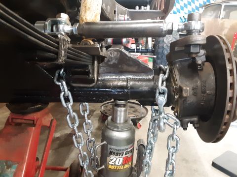 1985 Toyota Hilux - Close-up of a vehicle's front suspension and brake assembly, supported by a bottle jack and secured with chains.