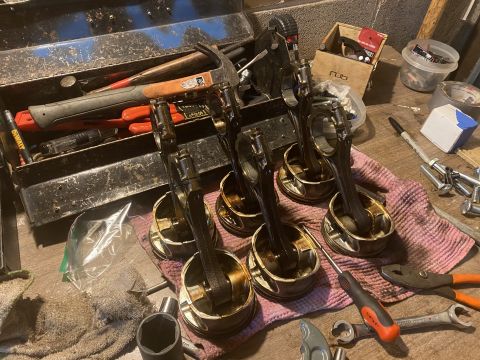 Six engine pistons with connecting rods laid out on a rag, next to a toolbox and various tools