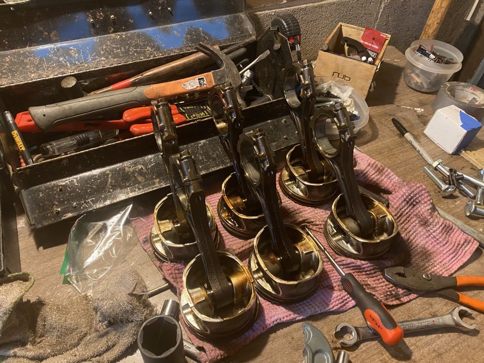 Six engine pistons with connecting rods laid out on a rag, next to a toolbox and various tools