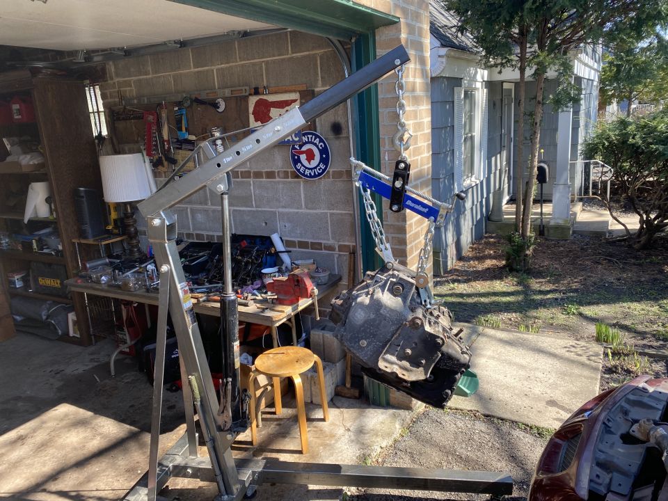 Transmission being lifted by an engine hoist in front of a garage