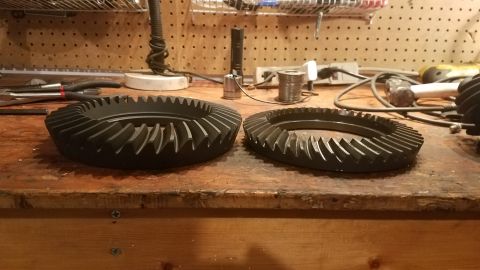 1985 Ford Bronco - Two differential ring gears are laid out on a wooden workbench, ready for installation or comparison.