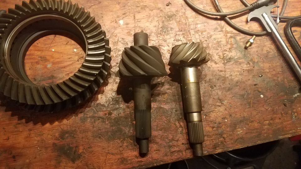 Ring gear and two pinion shafts on a wooden workbench. One shaft has '4.10' stamped on it