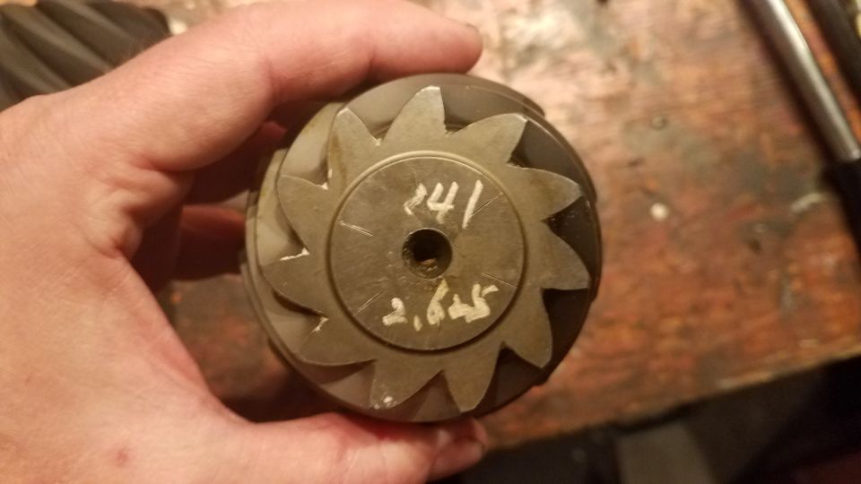 Hand holding a metal differential gear with markings '141' and '2,625' written on it