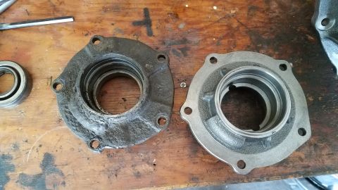 1985 Ford Bronco - Two bearing housings are shown on a wooden workbench. The housing on the left is dirty and worn, while the housing on the right appears to…
