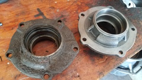 1985 Ford Bronco - Two metal bearing housings are shown on a wooden surface. The housing on the left is dirty and worn, while the housing on the right appears…