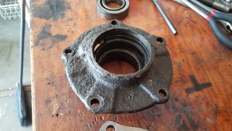 1985 Ford Bronco - A greasy, cast iron automotive part, possibly a bearing housing or flange, sits on a wooden workbench next to a bearing and some tools. The…