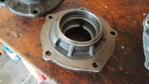 1985 Ford Bronco - A close-up view of a metal part, likely a hub or bearing housing, resting on a wooden surface. The part is cylindrical with a flanged base…