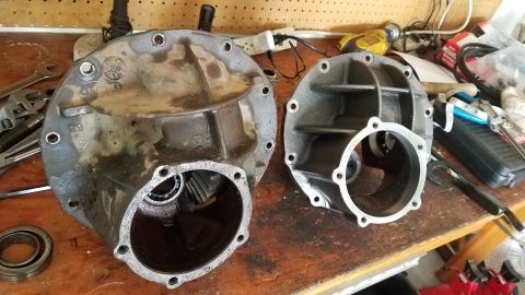 1985 Ford Bronco - Two differential housings are shown on a wooden workbench. The housing on the left is older and appears to be covered in grease, while the…