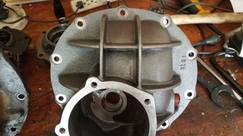 1985 Ford Bronco - A gray differential housing with multiple bolt holes is shown on a wooden surface. The housing has a ribbed, cast-iron appearance and a cir…
