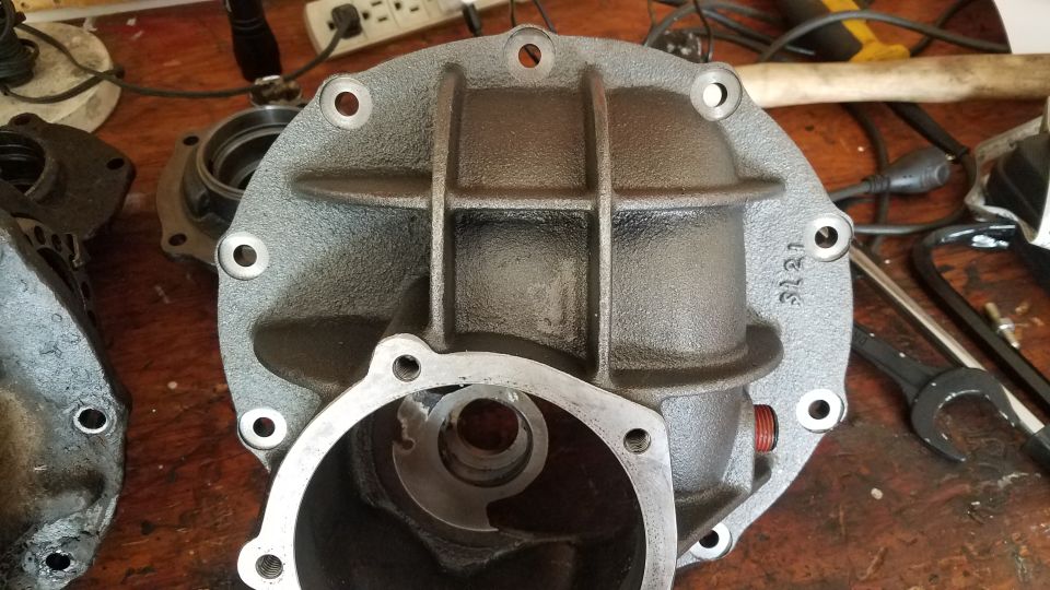 Gray differential housing with bolt holes and internal components on a wooden surface.