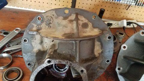 1985 Ford Bronco - A close-up view of a differential cover with various numbers and symbols cast into it. Several wrenches and bearings are visible in the for…