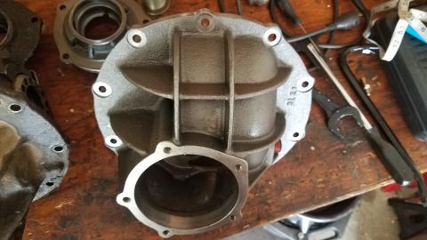 1985 Ford Bronco - A disassembled differential housing sits on a wooden workbench next to various tools, including wrenches and a tape measure. The housing is…