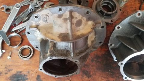 1985 Ford Bronco - A close-up view of differential housing parts and tools laid out on a wooden workbench. Several wrenches, a bearing, and a bolt are visible…