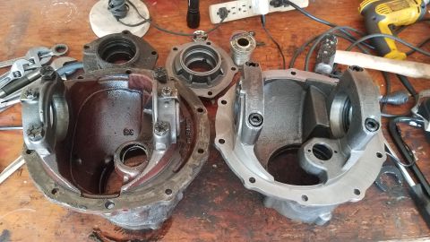 1985 Ford Bronco - Two differential housings are laid out on a wooden workbench, disassembled. Tools and electrical equipment are visible in the background.