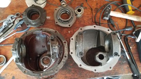 1985 Ford Bronco - Two differential housings are laid out on a wooden workbench alongside various tools including adjustable wrenches, a hammer, and a screwdr…