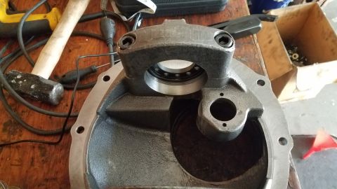 1985 Ford Bronco - A close-up view of a differential housing with a bearing installed, resting on a wooden workbench with tools and a cardboard box in the bac…