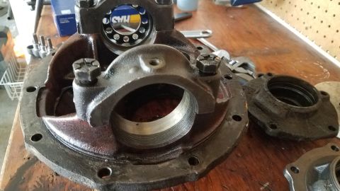 1985 Ford Bronco - A disassembled differential housing and related parts are laid out on a wooden workbench. The main housing shows threaded internal surfaces…