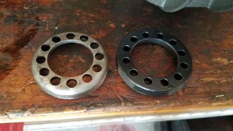 1985 Ford Bronco - Two circular metal parts with multiple holes are shown on a wooden surface. The part on the left is silver and appears to have threads, whi…