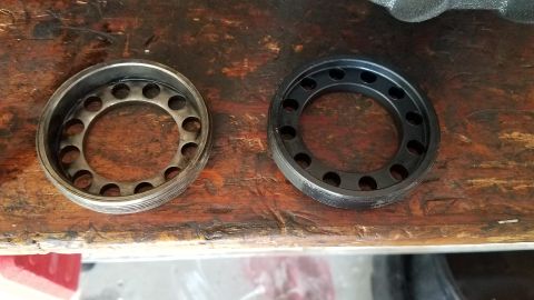 1985 Ford Bronco - Two circular metal parts with holes are shown on a wooden surface. The part on the left is silver and appears to be a bearing race, while t…