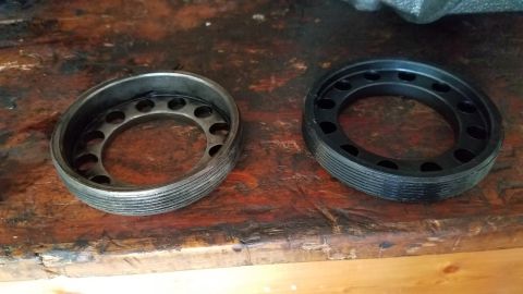 1985 Ford Bronco - Two circular metal and plastic parts with holes are shown on a wooden surface. The part on the left is silver and appears to be made of met…