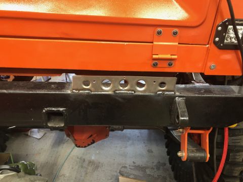 1992 Jeep Wrangler - A close-up view of the rear bumper and orange body panel of an off-road vehicle. A metal bracket with several circular cutouts is mounted t…