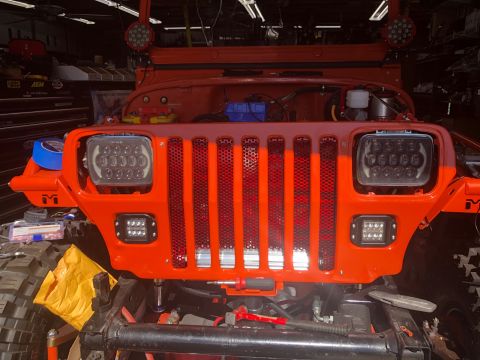 1992 Jeep Wrangler - The front end of an orange Jeep Wrangler is shown with aftermarket LED headlights and grille inserts. The vehicle appears to be in a garage…