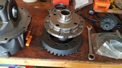 1985 Ford Bronco - A differential housing, ring gear, and spider gear assembly are laid out on a wooden workbench. Tools and parts boxes are visible in the ba…