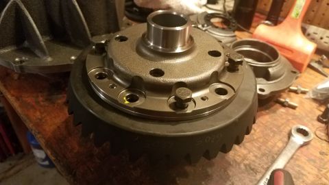 1985 Ford Bronco - A differential housing with a ring gear is shown on a wooden workbench, surrounded by tools and other parts. The ring gear has the number "…
