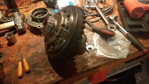 1985 Ford Bronco - A differential gear assembly and various tools, including a sledgehammer, wrenches, and screwdrivers, are laid out on a wooden workbench. T…