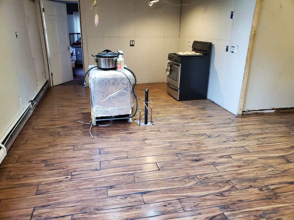 Unfinished kitchen area with a stove, slow cooker, and new wood-look flooring.